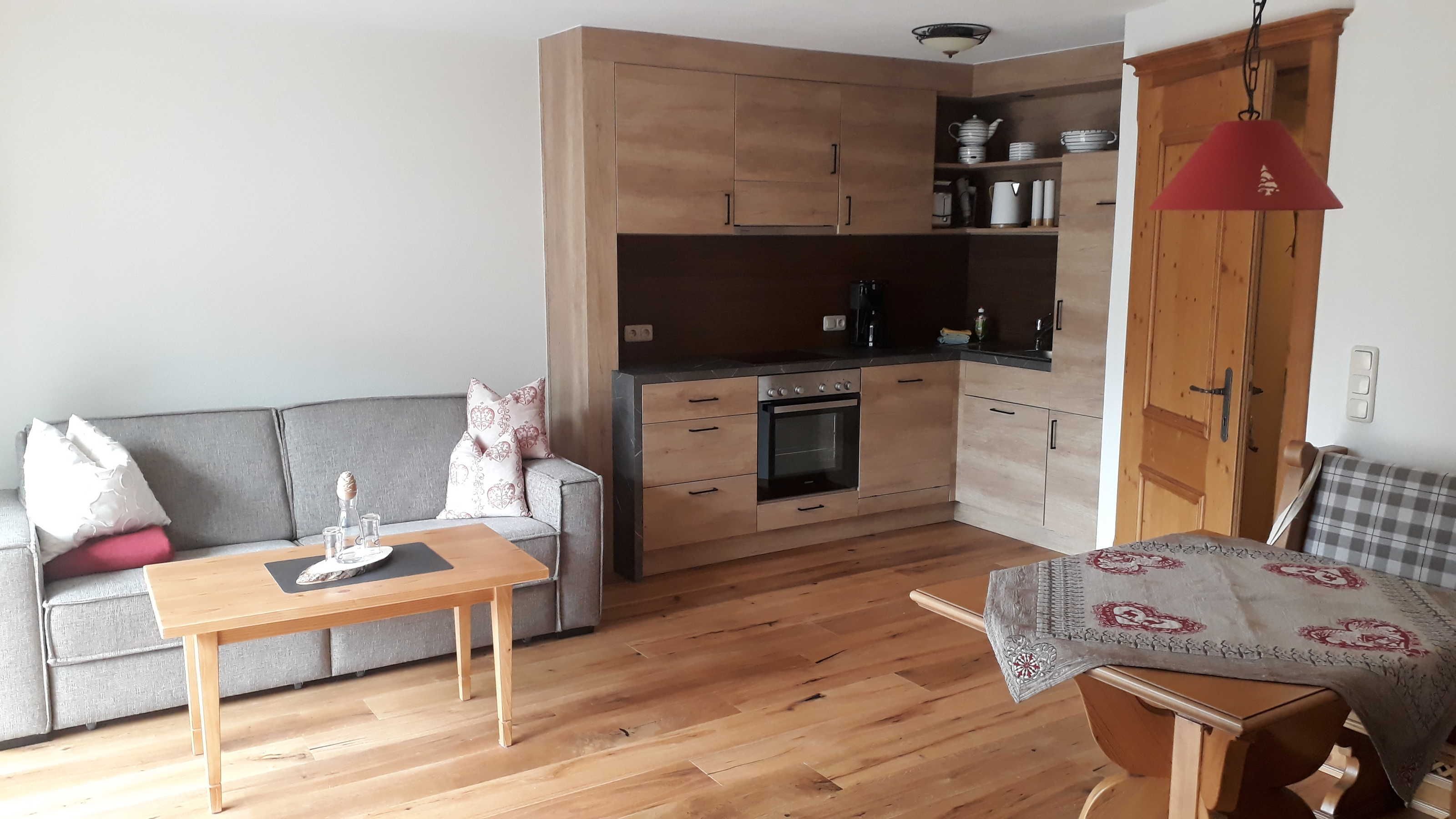 Un espacio habitable compacto con kitchenette, un sofá, una mesa de comedor y un cojín estampado en una silla.