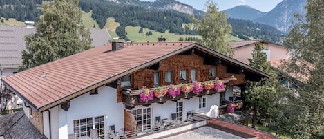 A chalet with a sloped roof, a balcony with flower boxes, and a view of mountains.