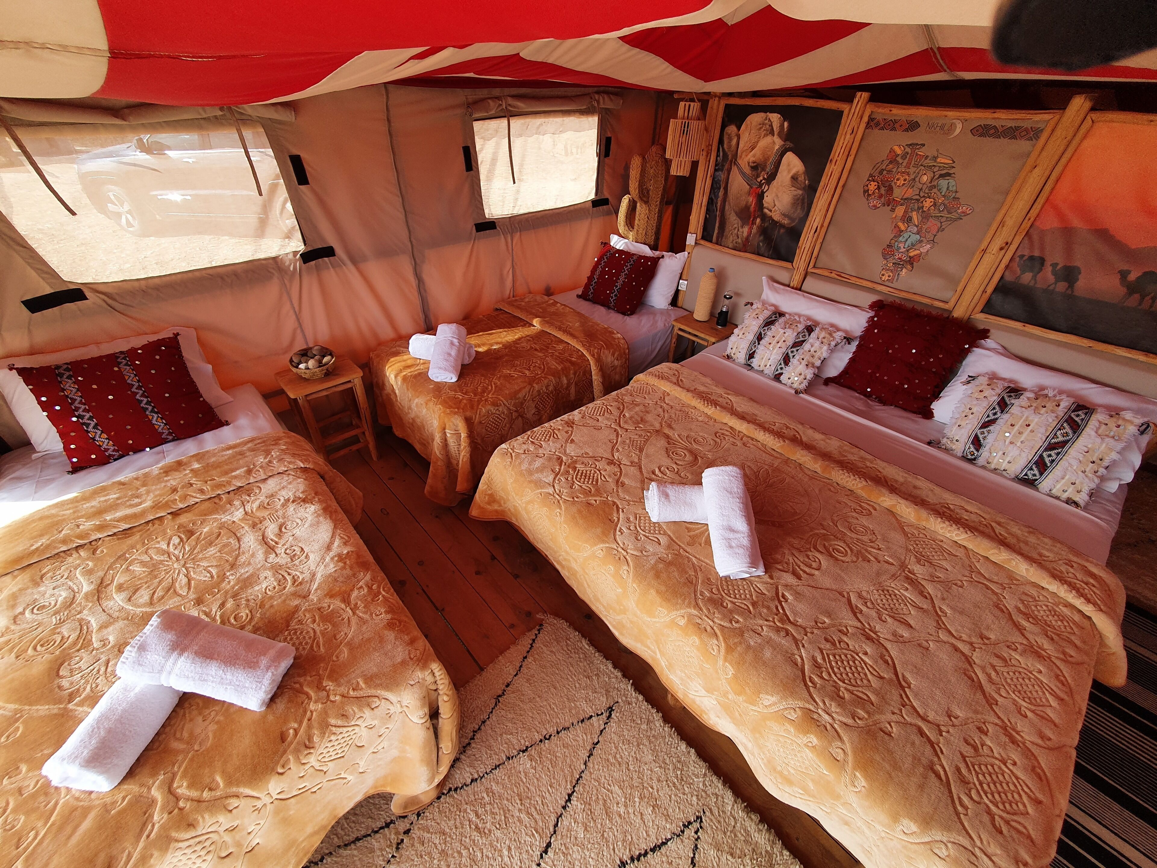 Una habitación acogedora y bien decorada con tres camas, cada una con una toalla doblada con cuidado. Hay almohadones decorativos, una mesita con una cesta y obras de arte en las paredes.