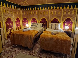 A room with two beds, each with a patterned bedspread and a rolled towel. The walls feature intricate patterns and designs, including palm trees and geometric shapes. - Nkhila Lodge - Agafay Luxury Tented Camp (Sidi Badhaj)