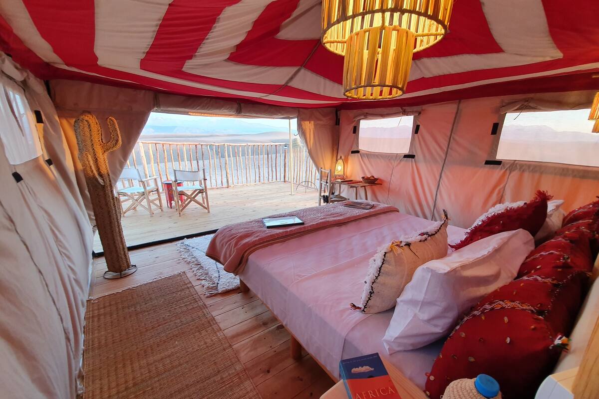 A tented room with a bed, pillows, a book, and a bottle.