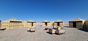 A row of beige tents with a pyramid roof, arranged in a line on a gravel surface. - Nkhila Lodge - Agafay Luxury Tented Camp (Sidi Badhaj)