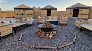 A circular seating area with sofas and a central fire pit, surrounded by a gravel ground. - Nkhila Lodge - Agafay Luxury Tented Camp (Sidi Badhaj)