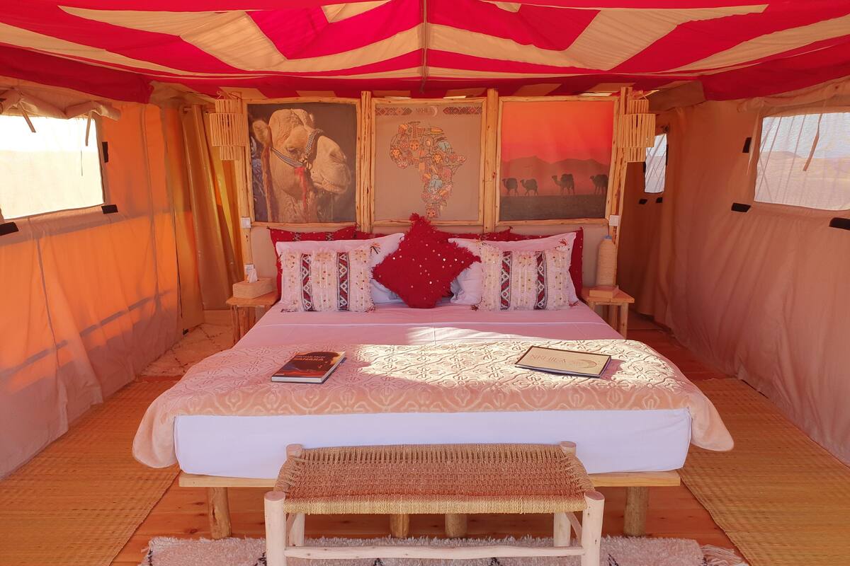A tented room with a bed, a bench, and a wall with a painting.