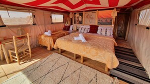 Una habitación con carpa, dos camas, una silla de madera y una pequeña mesa.