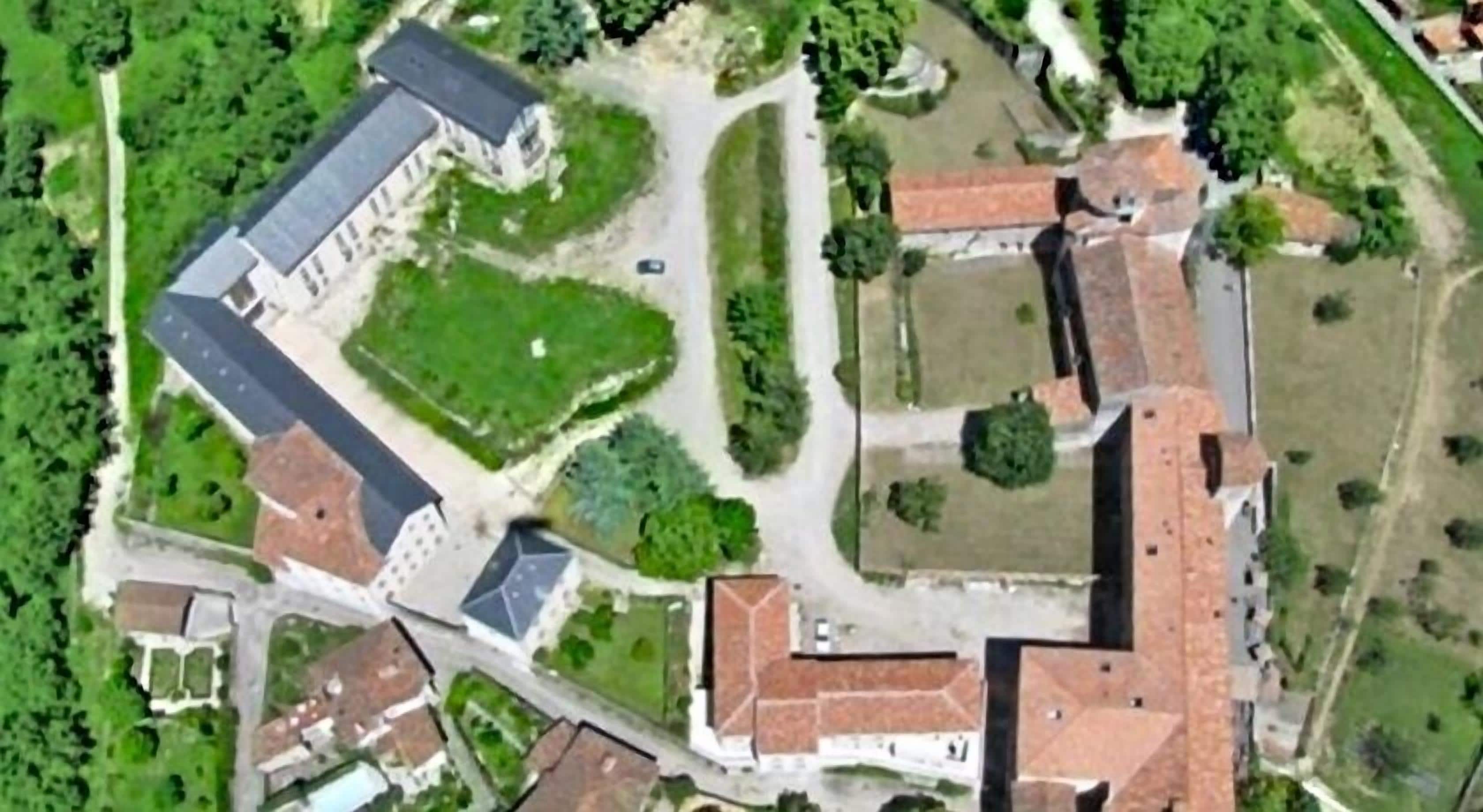 An aerial view of a historic building complex with multiple structures, including a large central building with a red roof and smaller adjacent buildings.