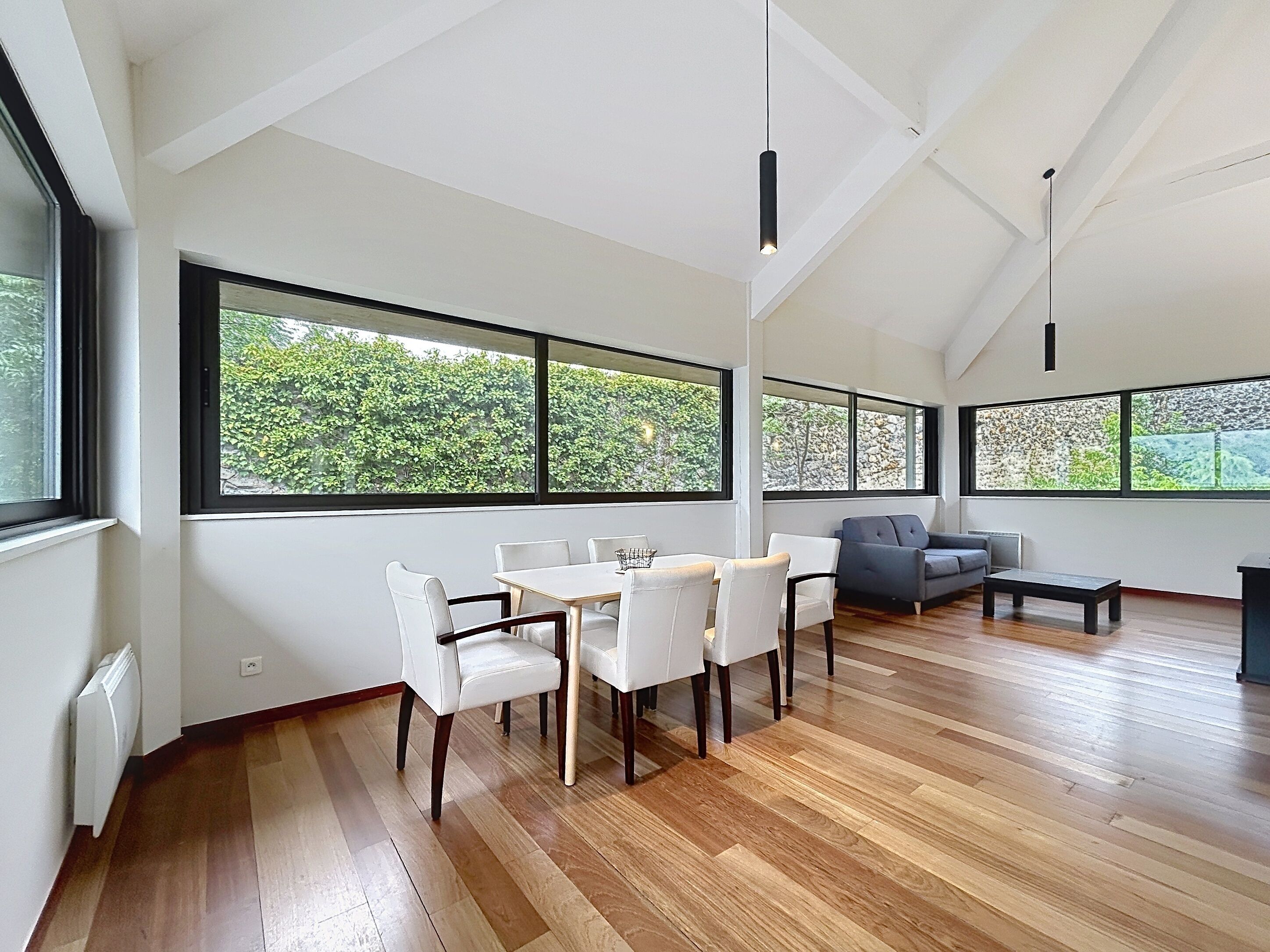 A modern living room with a dining area, large windows, and a sloped ceiling.