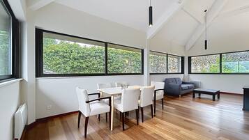 A modern living room with a dining area, large windows, and a sloped ceiling.