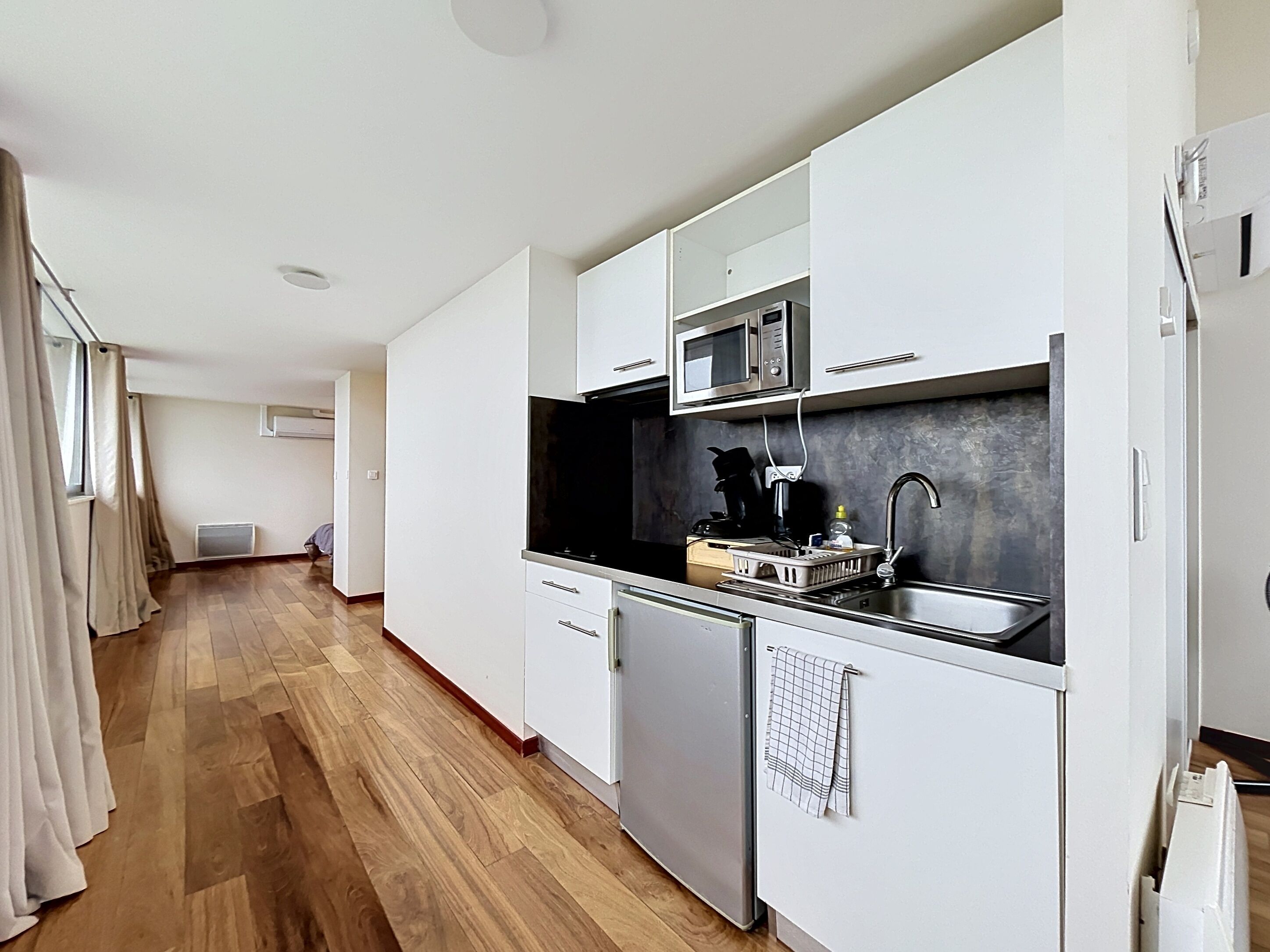 Una cocina moderna con armarios blancos, microondas integrado y pileta de acero inoxidable.