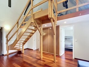 Eine Holztreppe mit Glastrennwand, die zu einem Erker mit Bett und Kleiderschrank führt.