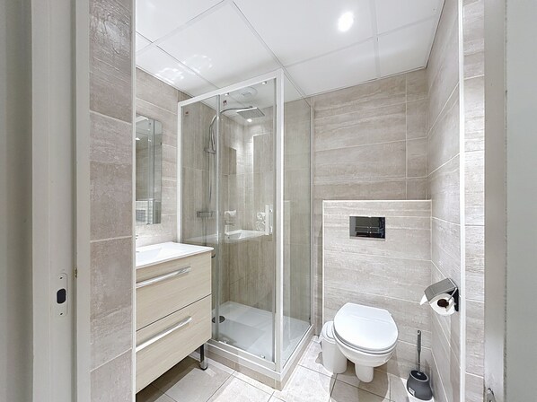 Un baño moderno con ducha envuelta en vidrio, inodoro y tocador con cajones.