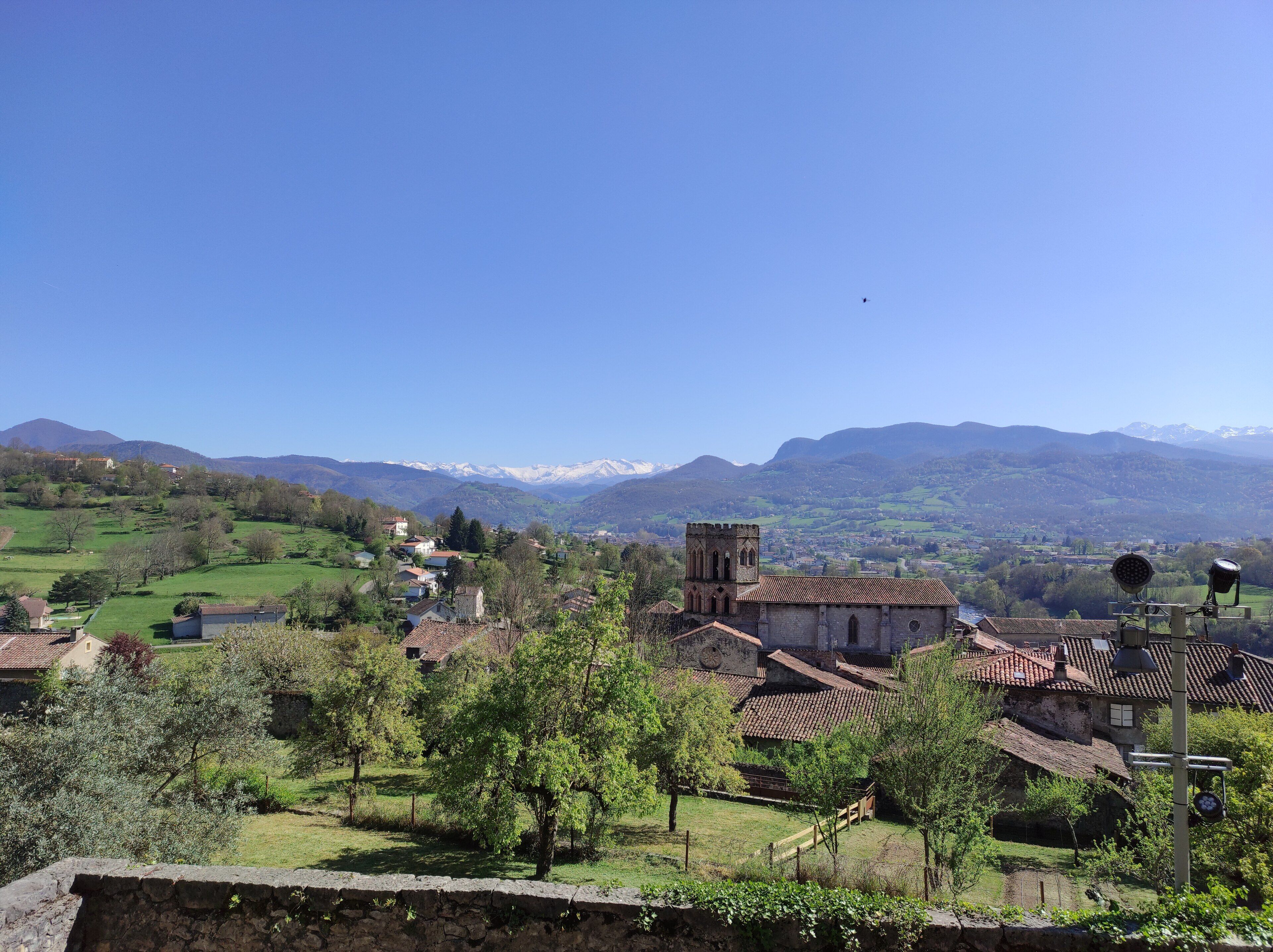 Un pueblo rural con edificios tradicionales, una iglesia con campanario y vistas a montañas distantes.
