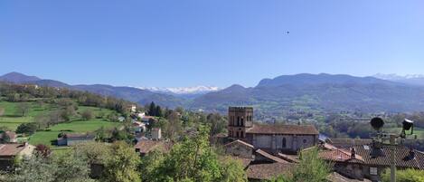 A rural village with traditional buildings, a church with a bell tower, and a view of distant mountains.