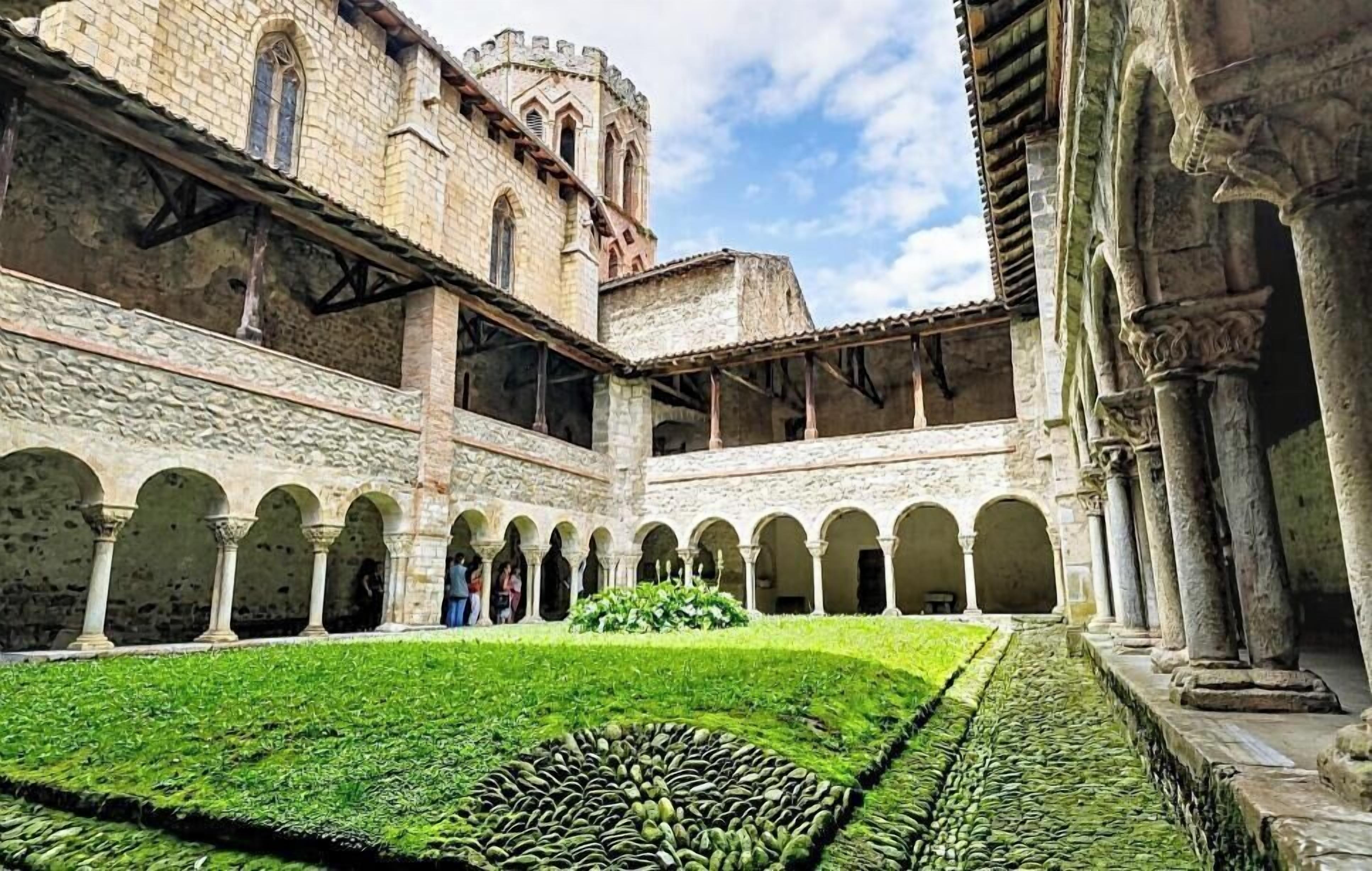 A courtyard with stone arches, a central garden, and a historic building with a tower.