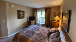 A hotel room with a bed, a television, a desk with a lamp, and a window with curtains.