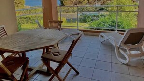 A balcony with a table and chairs, a view of greenery and a body of water.