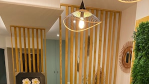 A modern interior with a wooden reception desk, a hanging light fixture, and a vertical wooden panel with a mirror and decorative items.