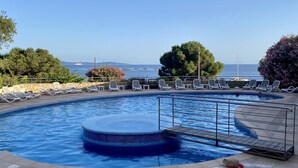 A swimming pool with a view of the sea, surrounded by lounge chairs and trees.