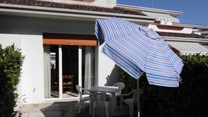 A patio with a striped umbrella, white plastic chairs, and a table.