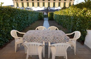 A covered patio area with a table and chairs, surrounded by neatly trimmed hedges. - Cozy villa with private garden-Beahost (Porto Santa Margherita)