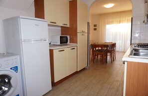 A compact kitchen with a washing machine, microwave, and a dining area with chairs and a table. - Cozy villa with private garden-Beahost (Porto Santa Margherita)