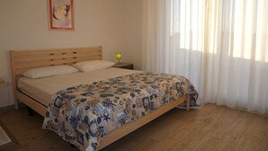 A bedroom with a wooden bed, a nightstand, a lamp, and a window with sheer curtains.