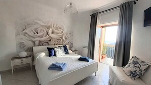 Une chambre à coucher avec un grand lit, une table de chevet, une lampe, une fenêtre avec des rideaux et une vue sur l’extérieur.