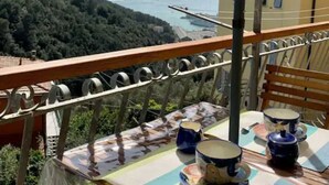 Un balcon avec une table dressée pour le thé, offrant une vue sur un paysage côtier avec des collines et la mer.