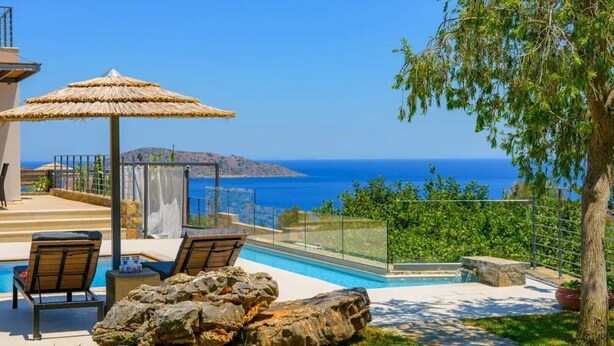 A pool area with lounge chairs and a pergola, overlooking a scenic view of the sea and hills. - Anemos Notos Villa (Nikolaos)