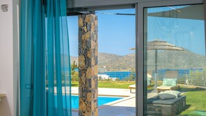 A modern living room with a large glass door leading to a pool and a scenic view. - Anemos Notos Villa (Nikolaos)