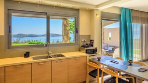 A modern kitchen with a large window, a dining area with a table and chairs, and a view of the sea. - Anemos Notos Villa (Nikolaos)