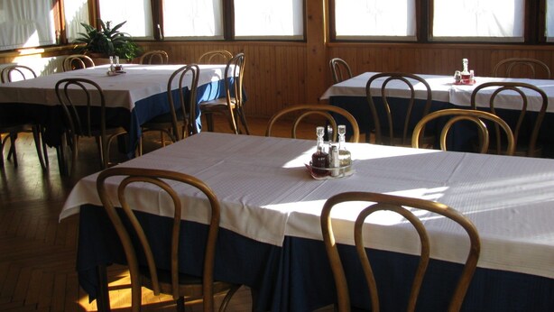 A restaurant with multiple tables, each with a white tablecloth and blue chair skirts. - Paradise for hikers. Family friendly. (Crni Vrh nad Idrijo)