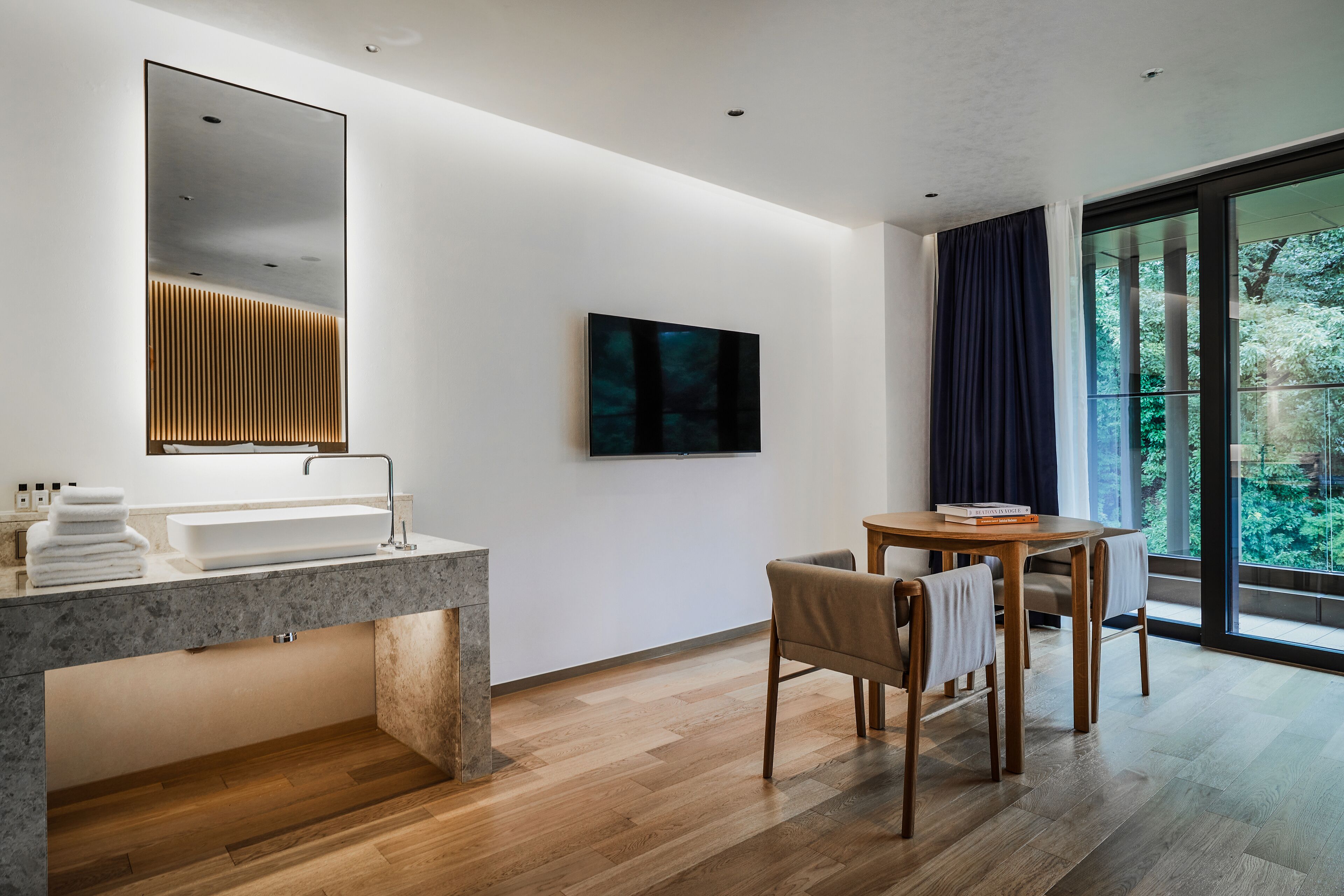 A modern bathroom with a large mirror, a sink, and a wooden floor.