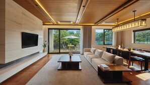 A modern living room with a flat-screen TV mounted on the wall, a wooden coffee table, a sofa, and a dining area with a table and chairs. - ANTO (Seoul)