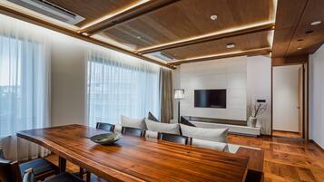 A modern conference room with a wooden table, comfortable seating, a flat-screen TV, and a large window with sheer curtains.
