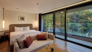 A modern hotel room with a large bed, a sofa, a wooden coffee table, and a large window offering a view of a garden. - ANTO (Seoul)