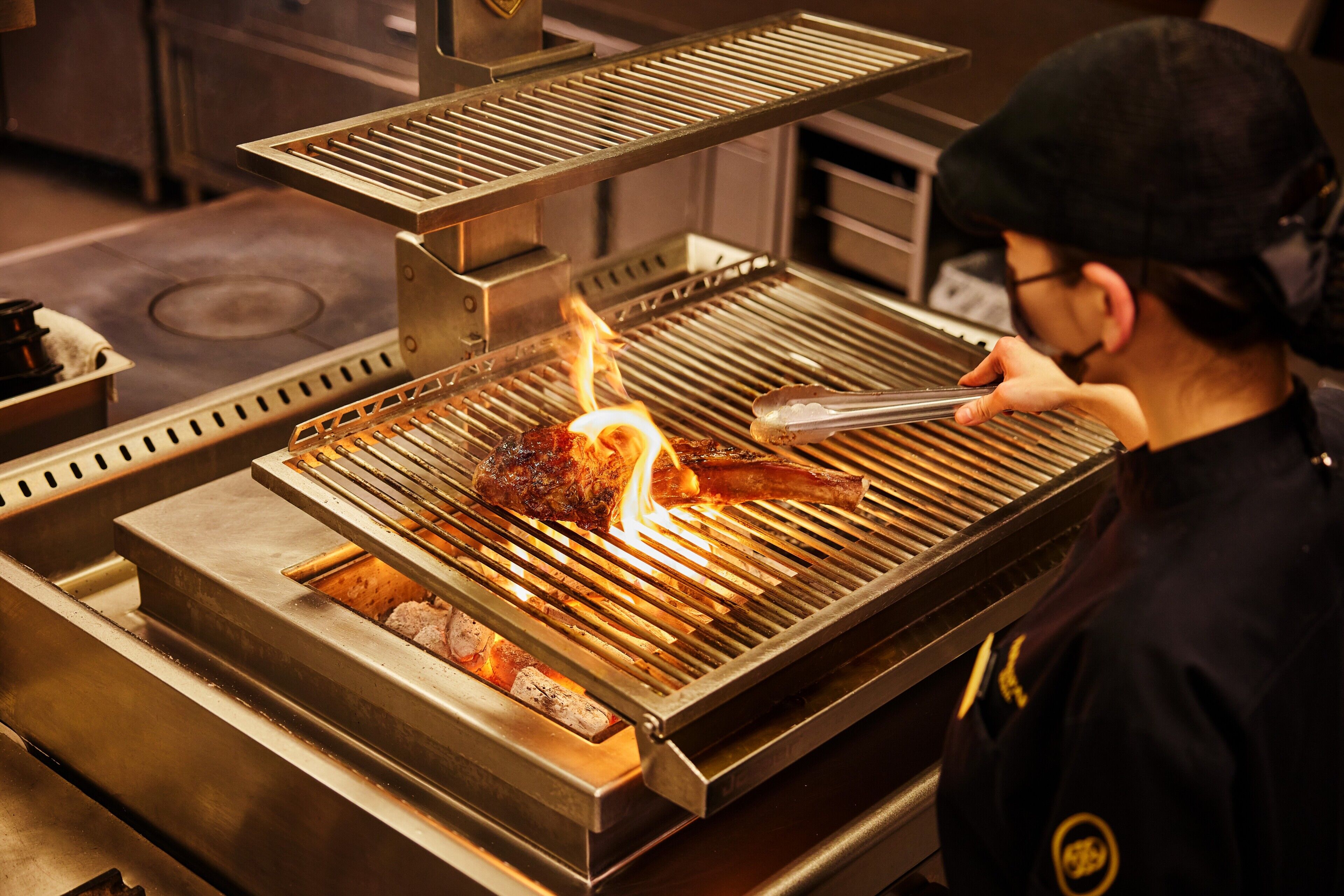 Une personne est en train de faire griller de la viande sur un barbecue en acier inoxydable dans une cuisine.