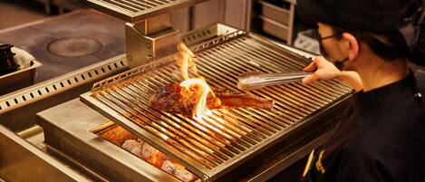 Une personne est en train de faire griller de la viande sur un barbecue en acier inoxydable dans une cuisine.