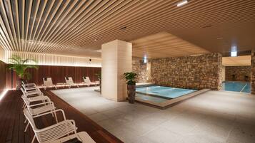 A modern indoor pool area with lounge chairs, a stone wall, and a wooden ceiling.