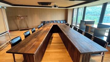 A conference room with a long wooden table, black chairs, and a projector screen.