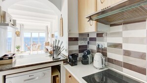 A modern kitchen with a view of the sea, a coffee maker, and a kettle on the counter. - STA BARBARA 27 Roses (Rosas / Roses)