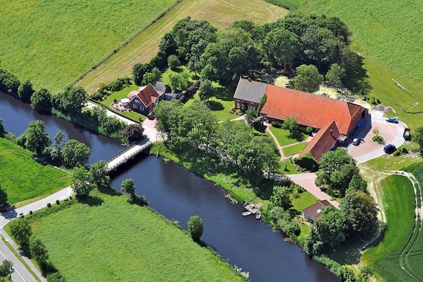 An aerial view of a riverside property with a main house, smaller buildings, and a bridge over the river.