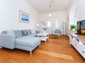En moderne stue med en grå hjørnesofa, et hvidt sofabord og et fjernsyn på et træstel.