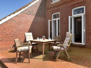 En terrasse med murstensvæg, et træbord og fire stole.