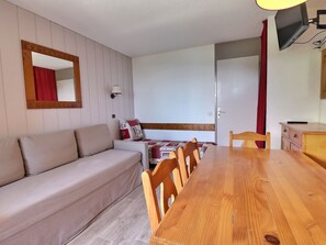 Um quarto aconchegante com uma mesa de jantar de madeira, um sofá, um espelho e uma televisão.