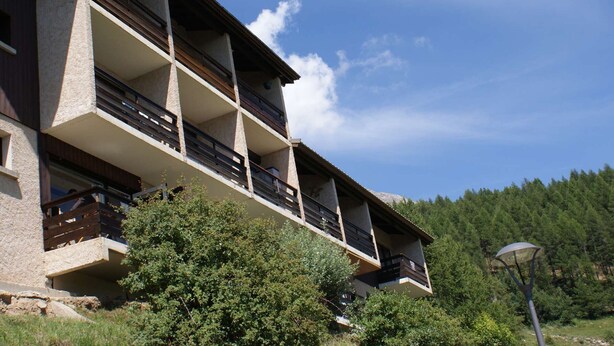A multi-story building with balconies, surrounded by trees and a clear sky.