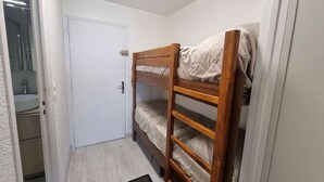A small, narrow room with a bunk bed, a door, and a bathroom visible through a glass door.