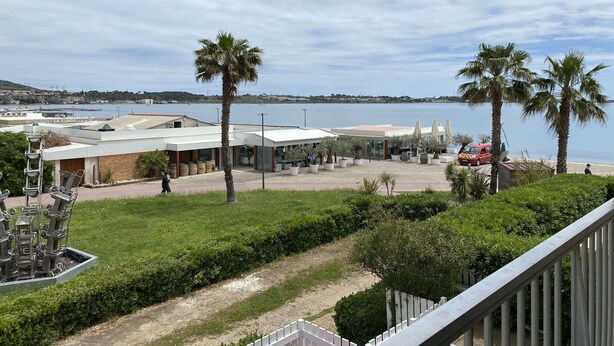 A coastal view with a restaurant, palm trees, and a clear sky.