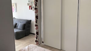 A room with a grey sofa, a bed with a patterned bedspread, and a wardrobe with a white door.