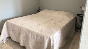 A neatly made bed with a floral-patterned bedspread in a room with light-colored walls and a small bedside table with a lamp.